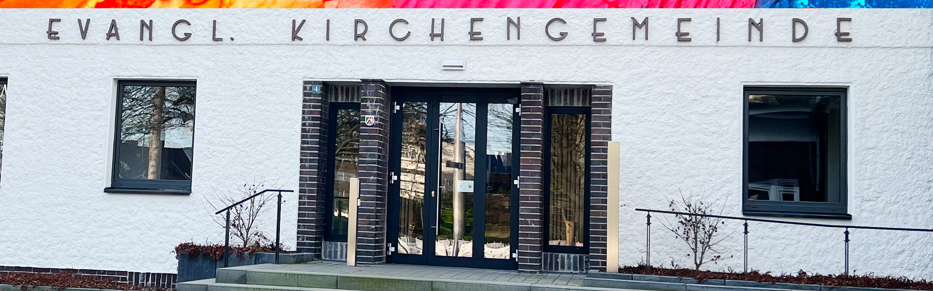Eingang einer Evangelischen Kirchengemeinde mit bunten Streifen darüber.