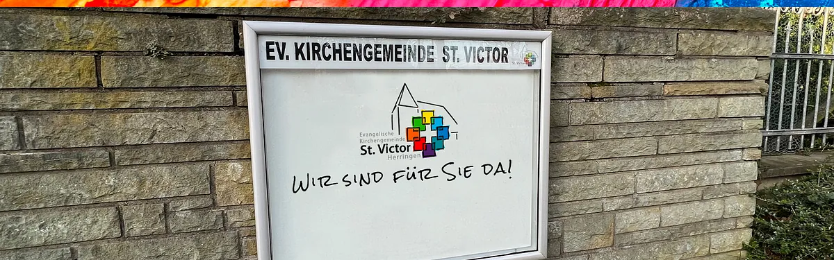 White sign with a colorful logo and text, set against a blurred stone wall.