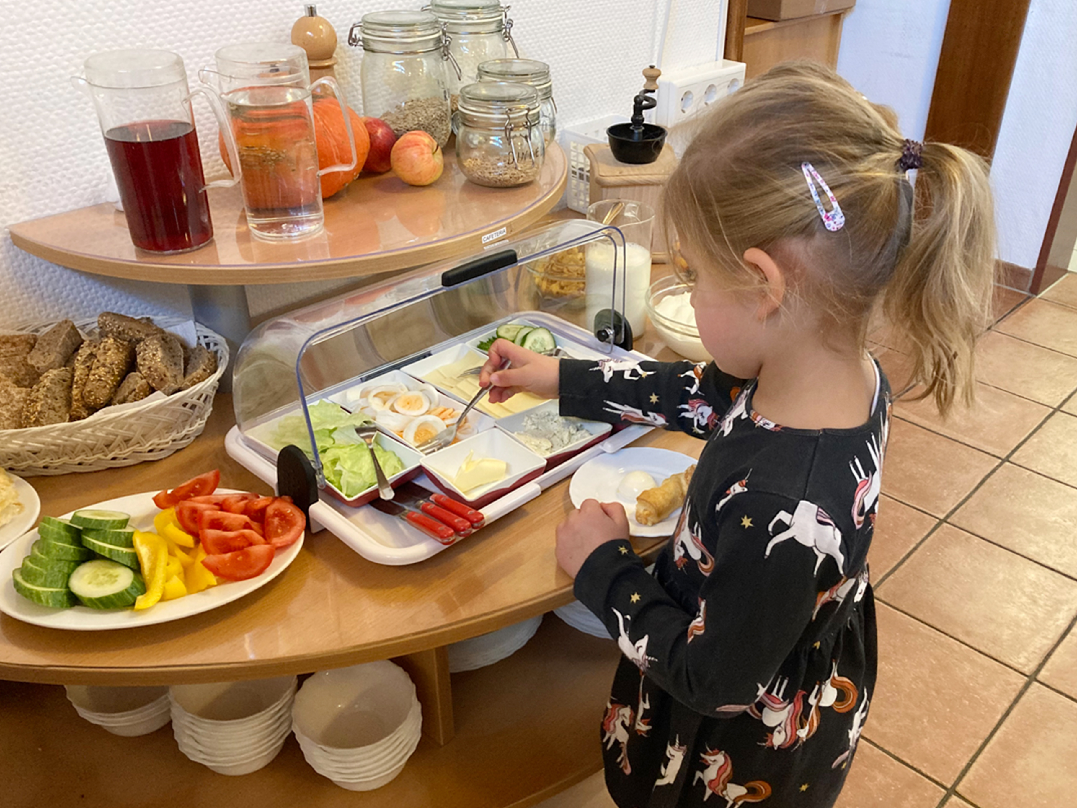 Ein kleines Mädchen bedient sich an einem Buffet mit Speisen und Getränken.
