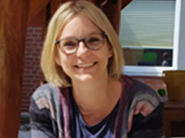 Porträt einer lächelnden Frau mit Brille und gestreiftem Cardigan.