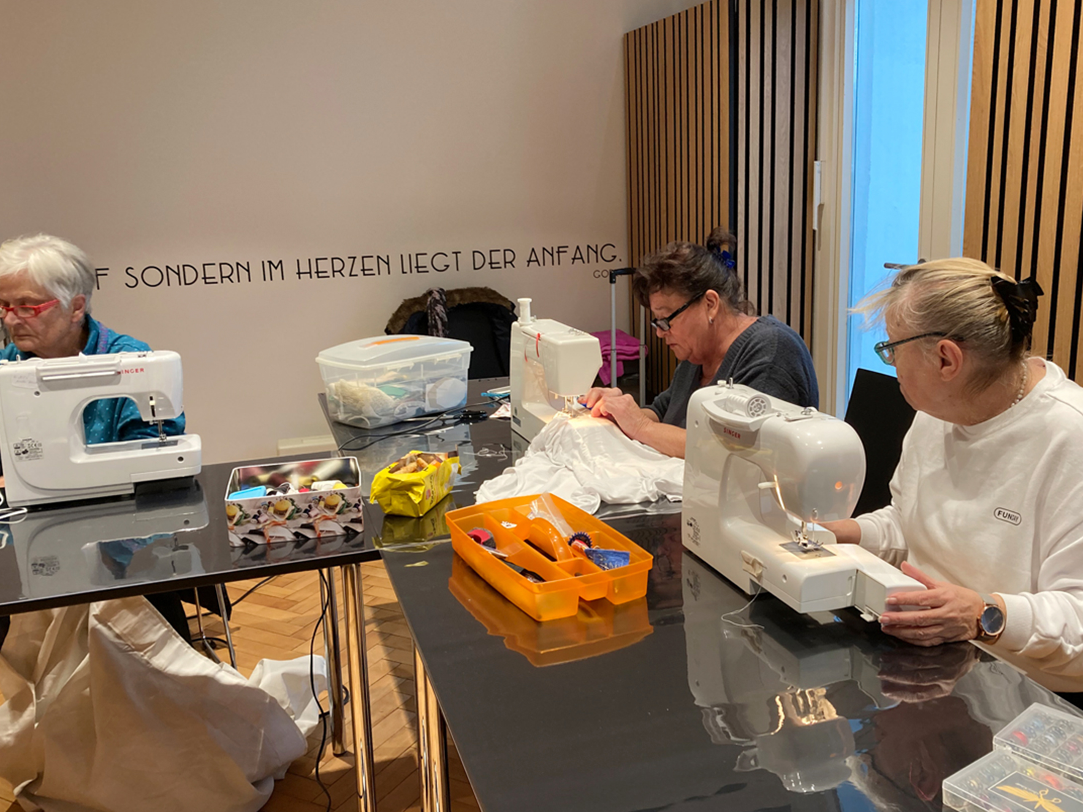 Mehrere Frauen nähen an Nähmaschinen an einem Tisch.