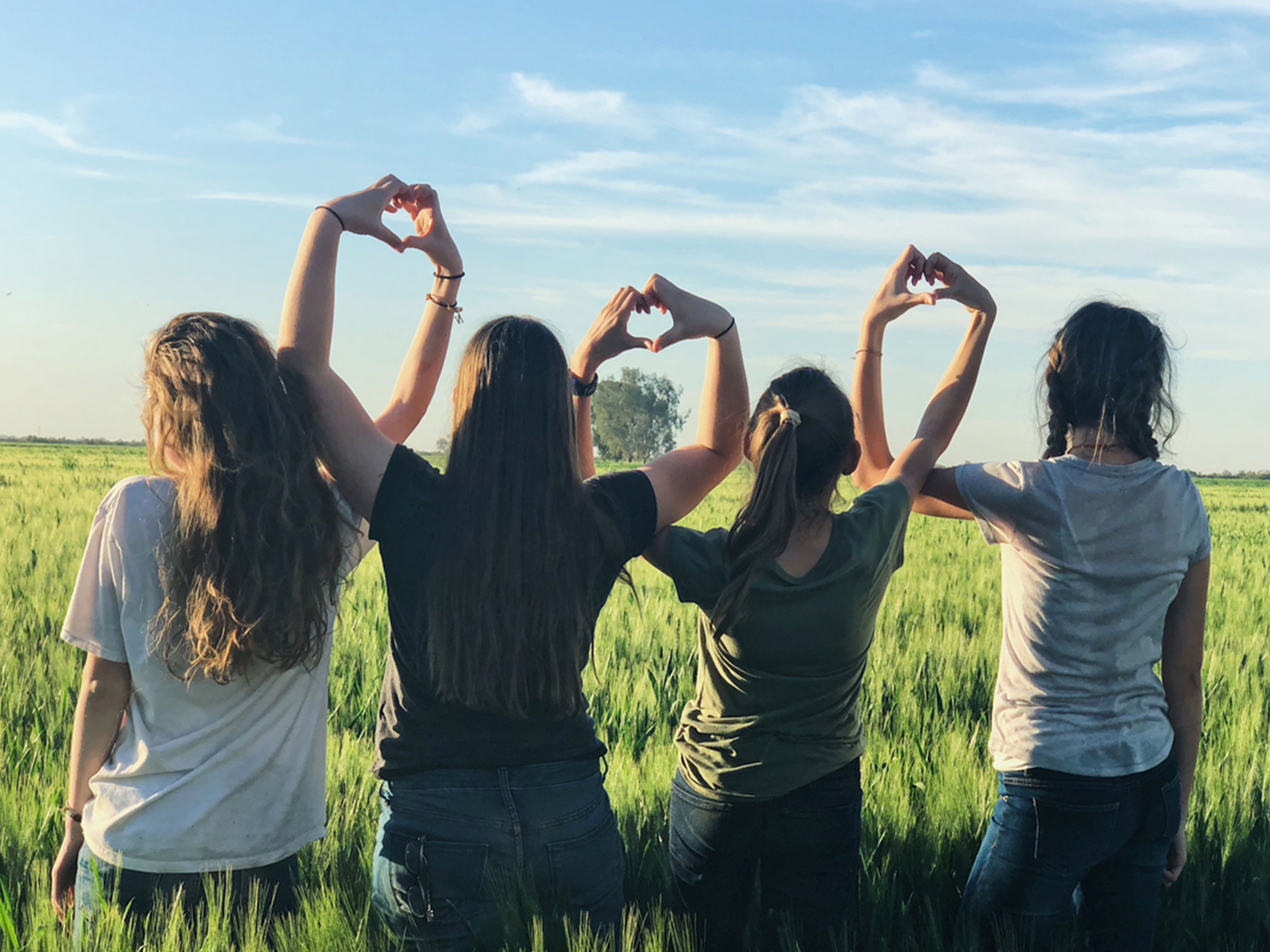 Vier Personen bilden mit den Händen Herzen vor einem grünen Feld.