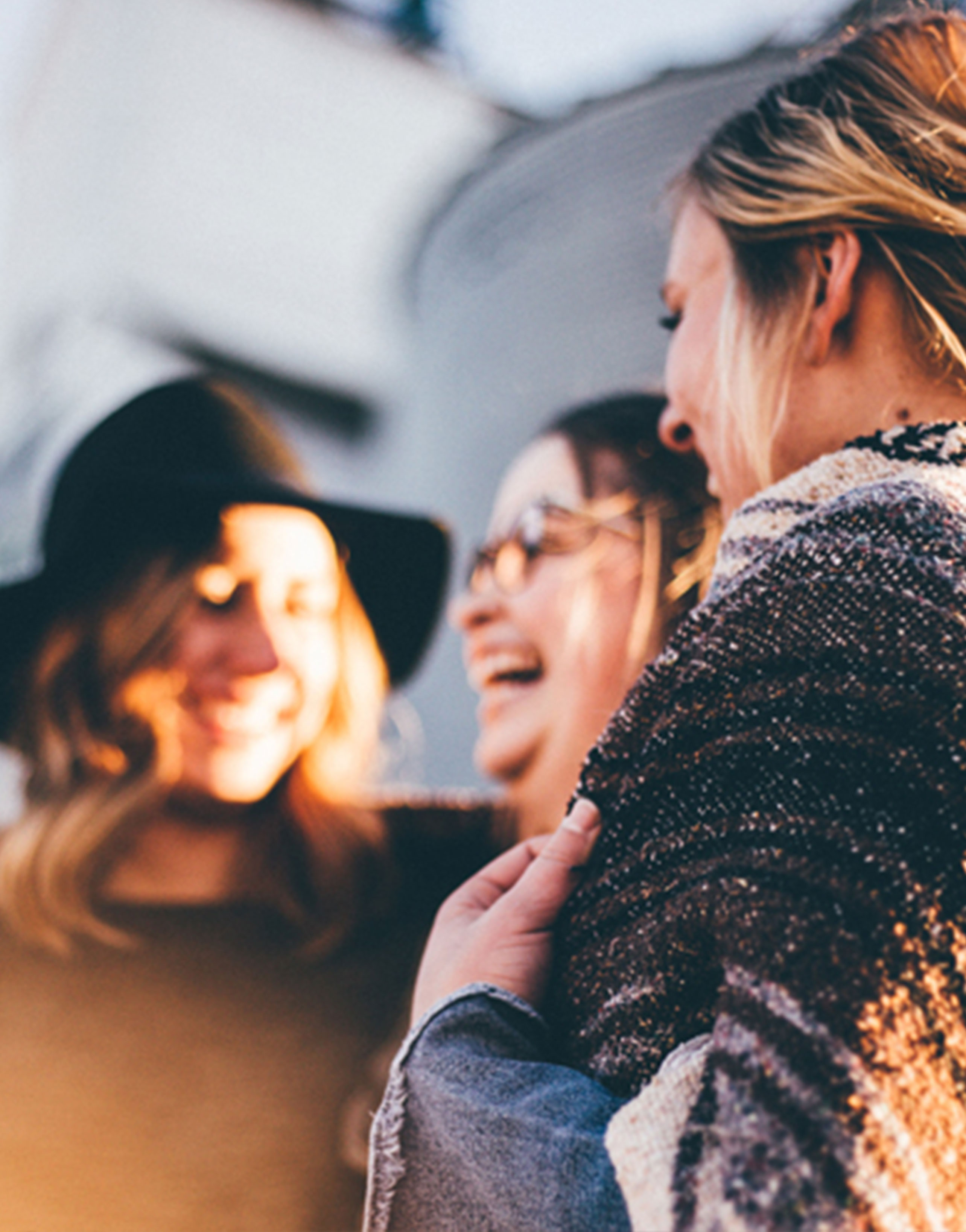Drei lächelnde Frauen umarmen sich im Freien.