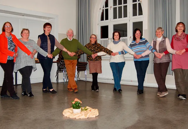 Eine Gruppe von neun Personen tanzt Hand in Hand in einem Kreis.