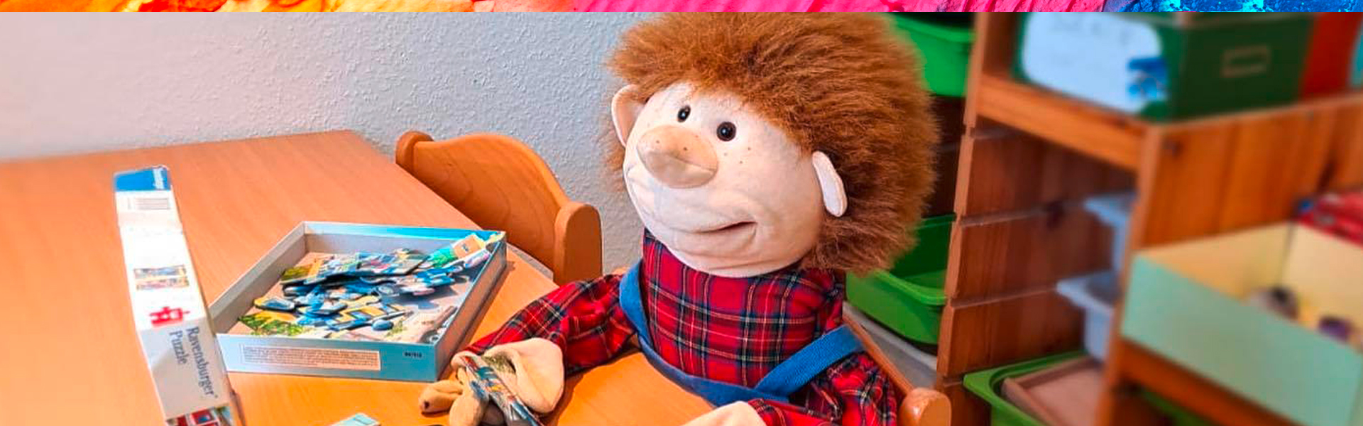 Eine Puppe mit rotem Karohemd sitzt an einem Tisch mit einem Spiel.